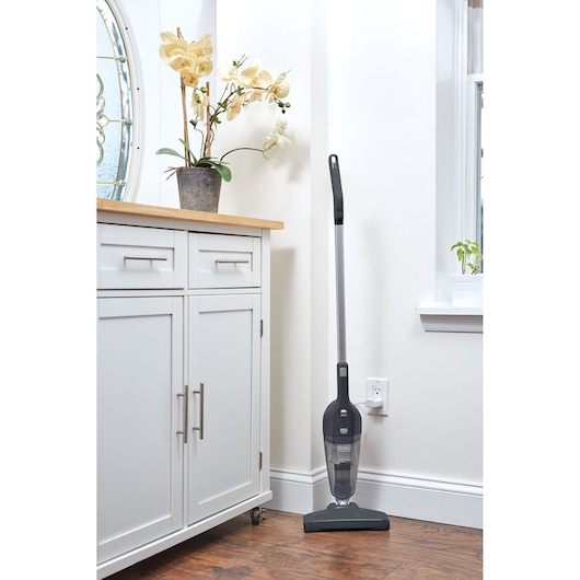 BLACKDECKER NSVA315J stick vacuum cleaner shown upright in a corner on hardwood floor, side angle.