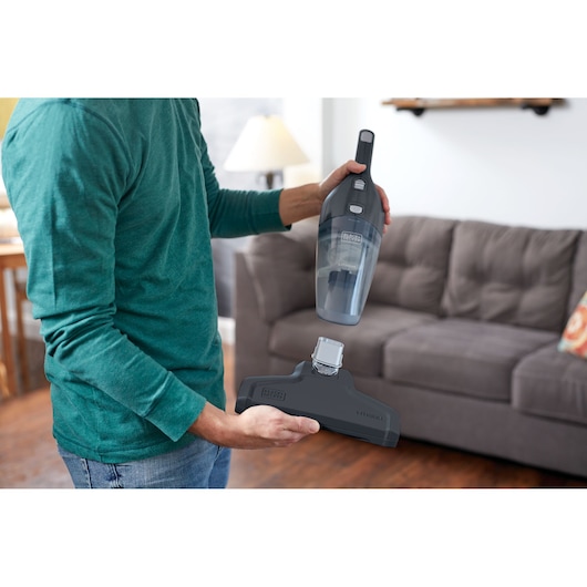 BLACKDECKER NSVA315J handheld vacuum and detachable brush held by a person in a living room.