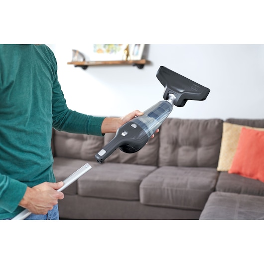 BLACKDECKER NSVA315J handheld vacuum with wide nozzle shown in a living room setting.