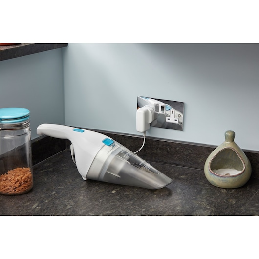 BLACKDECKER NVC115JL handheld vacuum white and blue charging on kitchen countertop, angled side view.