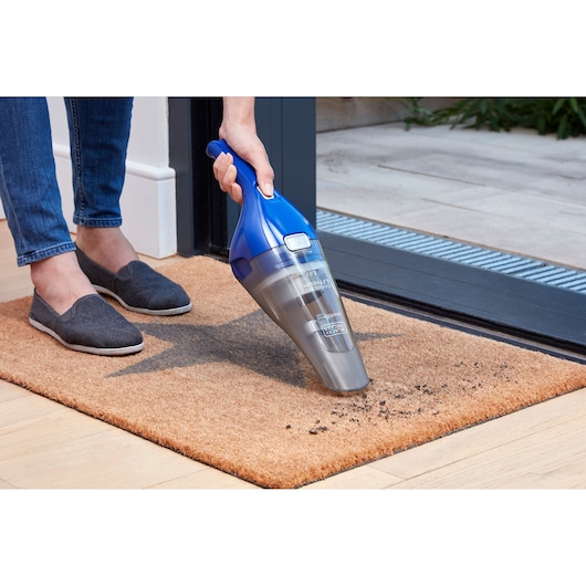 BLACKDECKER NVC115WA handheld vacuum cleaning dirt from entrance mat, outdoor setting.