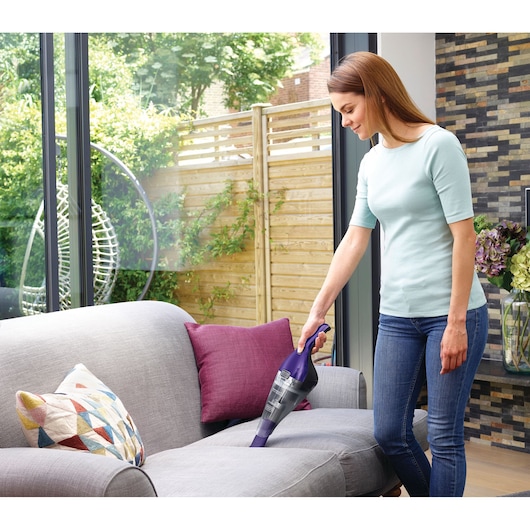 BLACKDECKER NVC215WP handheld vacuum cleaning grey sofa in living room.