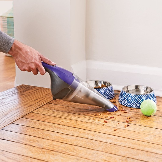 BLACKDECKER NVC215WP handheld vacuum cleaner picking up pet food crumbs near pet bowls on hardwood floor.