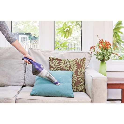 BLACKDECKER NVC215WP handheld vacuum cleaning pet hair from a blue cushion on a sofa.