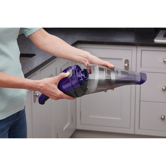 BLACKDECKER NVC215WP handheld vacuum with purple and gray design shown being emptied in a kitchen setting.