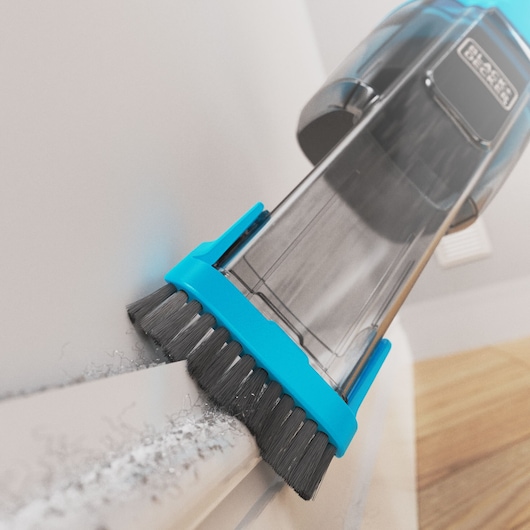 Photo of BLACK+DECKER NVD215J handheld vacuum cleaning dust from a corner with blue brush attachment.