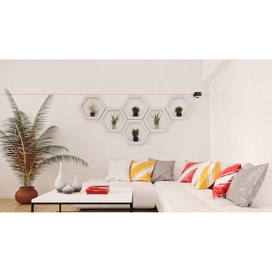 BLACKDECKER REVBDLL100 laser level projects a red line across a living room wall above white shelves with plants.