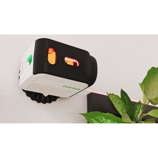 Photo of BLACK+DECKER REVBDLL100 laser level in black and white mounted on a wall near a green plant.