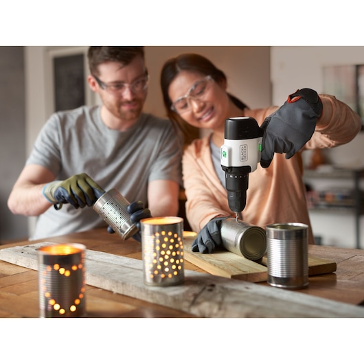 BLACKDECKER REVHD12C cordless drill used to make holes in metal cans for decorative lanterns, indoor setting.