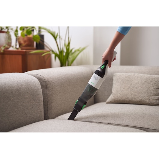 BLACKDECKER REVHV8C handheld vacuum cleaner in use on a gray sofa in a living room setting.