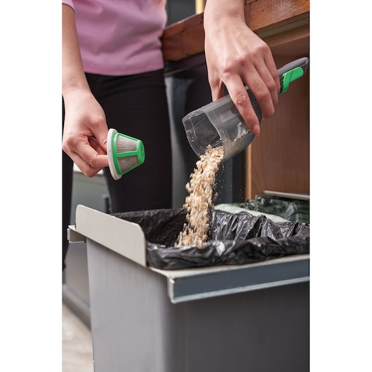 BLACKDECKER REVHV8C handheld vacuum being emptied into trash bin, filter removed, indoor setting