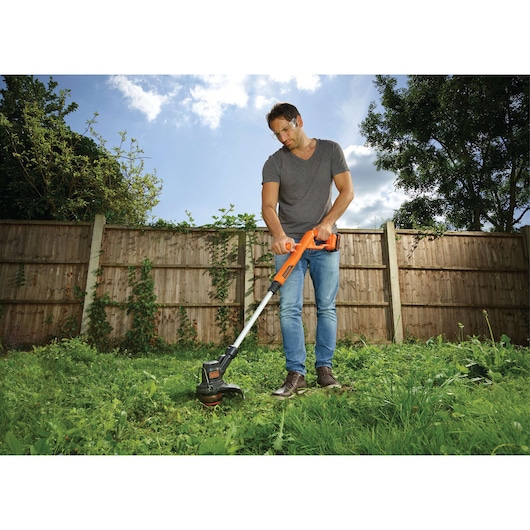 Photography of BLACKDECKER ST1823 orange cordless grass trimmer in use outdoors.