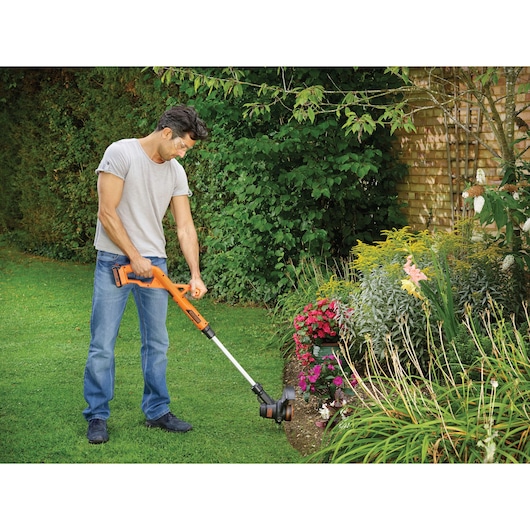 BLACKDECKER ST1823 grass trimmer in use trimming lawn edge near flower bed outdoors.