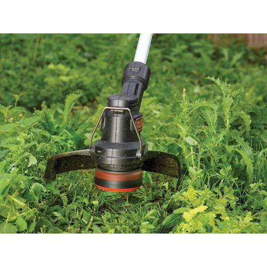 BLACKDECKER ST1823 grass trimmer head in action trimming green weeds outdoors.