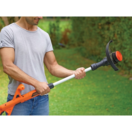 Person holding BLACKDECKER ST1823 orange and black grass trimmer with telescopic shaft in a garden.