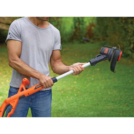 BLACKDECKER ST1823 grass trimmer with orange handle shown in use outdoors.