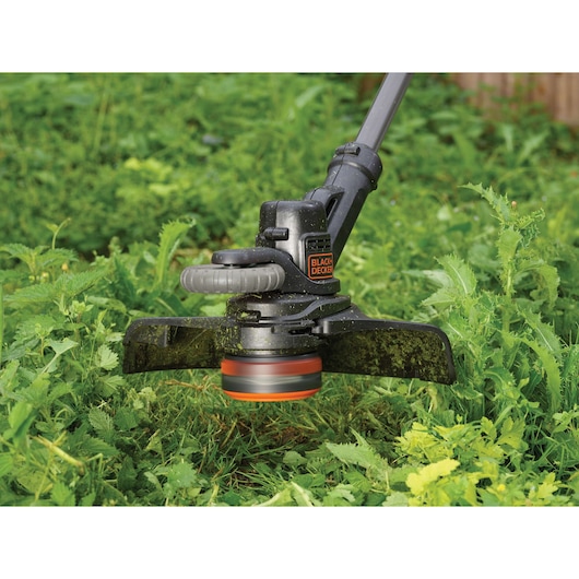 BLACKDECKER cordless grass trimmer STC1820PC cutting green weeds outdoors.