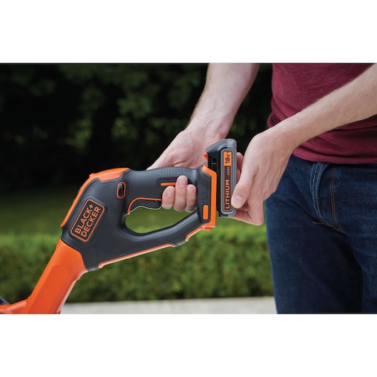 BLACKDECKER STC1820PC grass trimmer, close-up of handle and 18V lithium battery installation outdoors.
