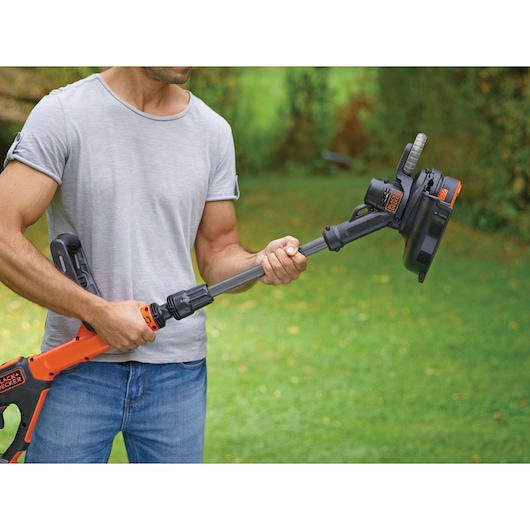 BLACKDECKER STC1820PC grass trimmer held by person outdoors, orange and black design.