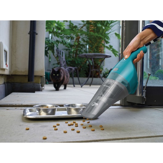 BLACKDECKER WDB115WA handheld vacuum cleaning pet food near metal bowls, indoor setting.