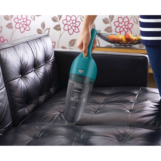BLACKDECKER WDB115WA handheld vacuum with teal top cleaning black leather sofa.