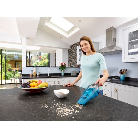 BLACKDECKER WDC215WA handheld vacuum cleaning cereal from kitchen counter, fruits bowl visible.