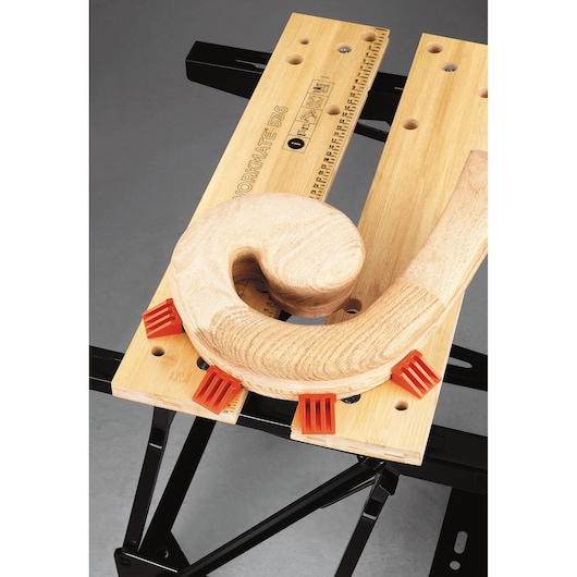 Photo of BLACKDECKER WM536 workbench with wooden workpiece clamped by orange grips, top-down angle.